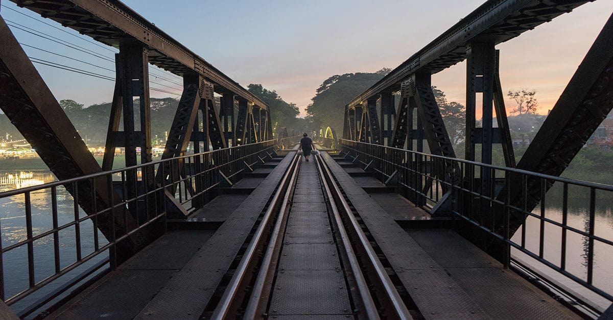 Nice view of the bridge on River Kwai with people walking on it during the sunset.